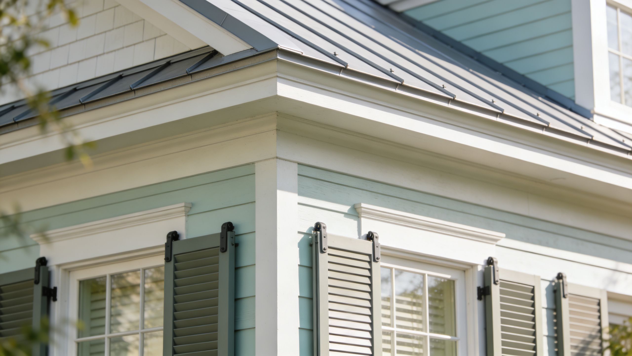 A close-up of the architectural details of a light blue coastal home with sage green shutters.